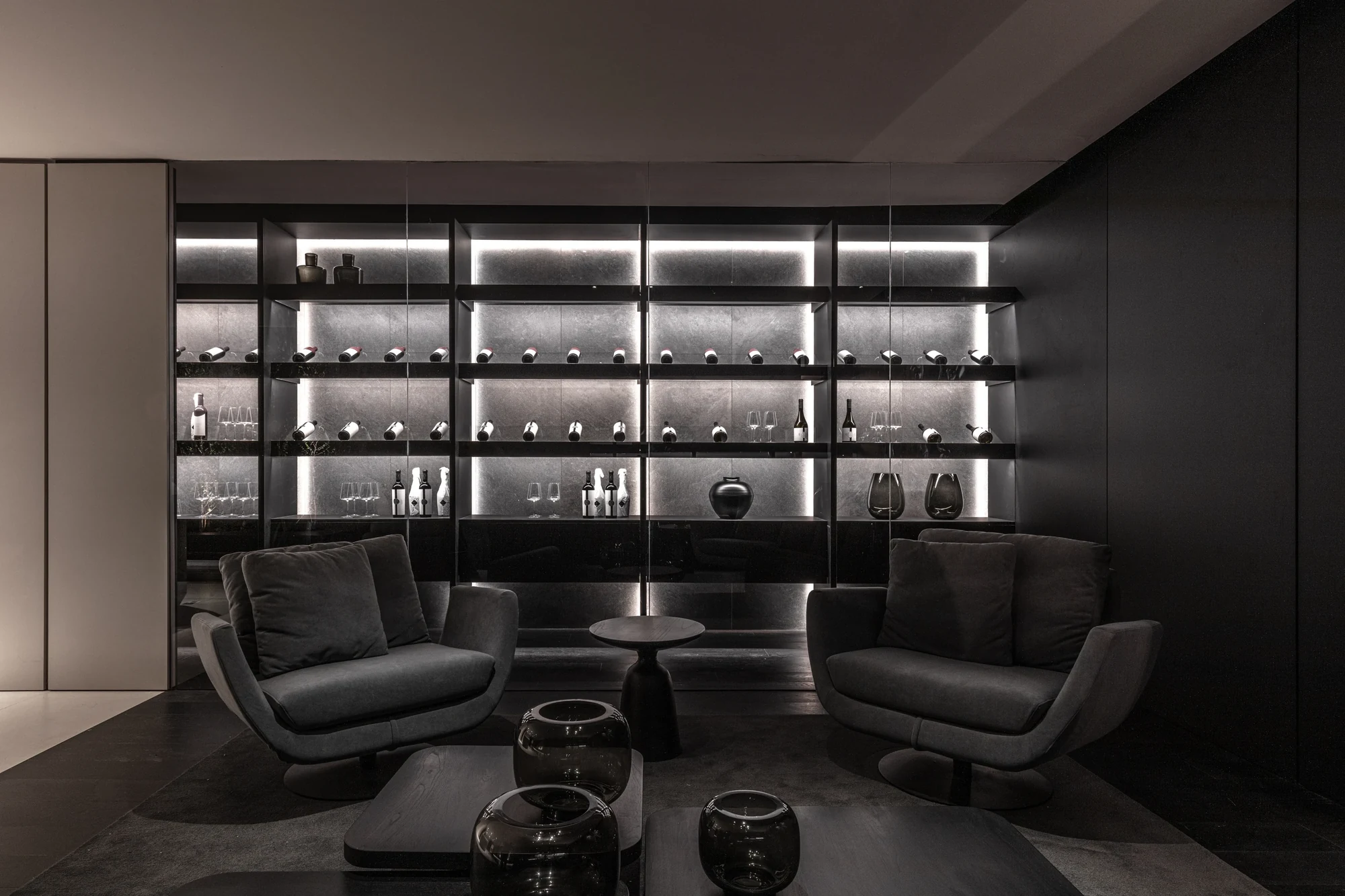 Cava vidriada iluminada con sillones, en un estar de tonos oscuros