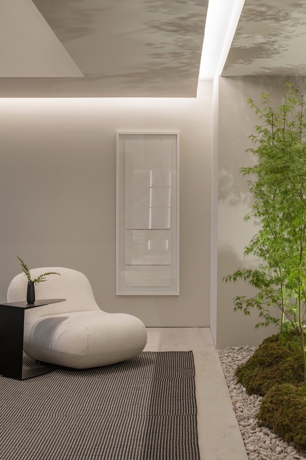 Sillón bouclé blanco frente al jardín interior de arce, con una obra enmarcada en la pared