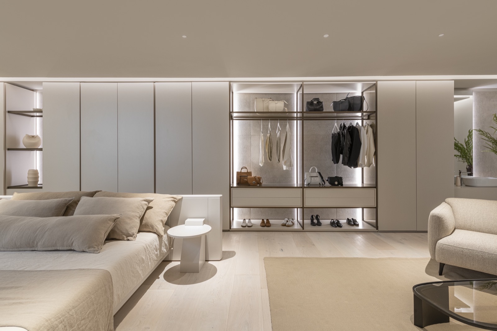Dormitorio abierto al vestidor, con estantes y barrales iluminados sobre revestimiento de piedra