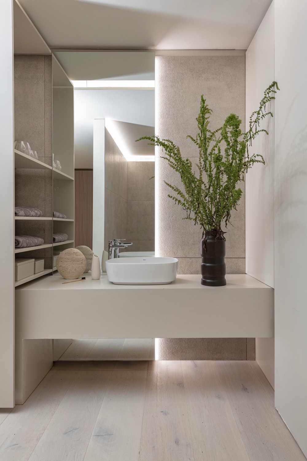 Baño con bacha de apoyo, espejo integrado y revestimiento de piedra con luz rasante