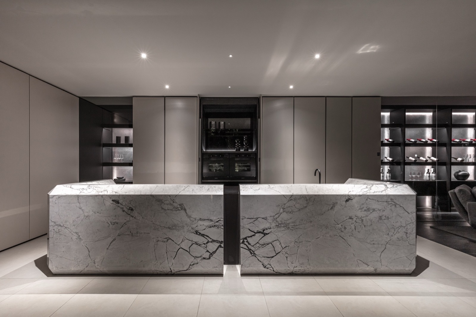 Cocina con isla de mármol de gran porte, frentes continuos sin tiradores y cava iluminada al fondo