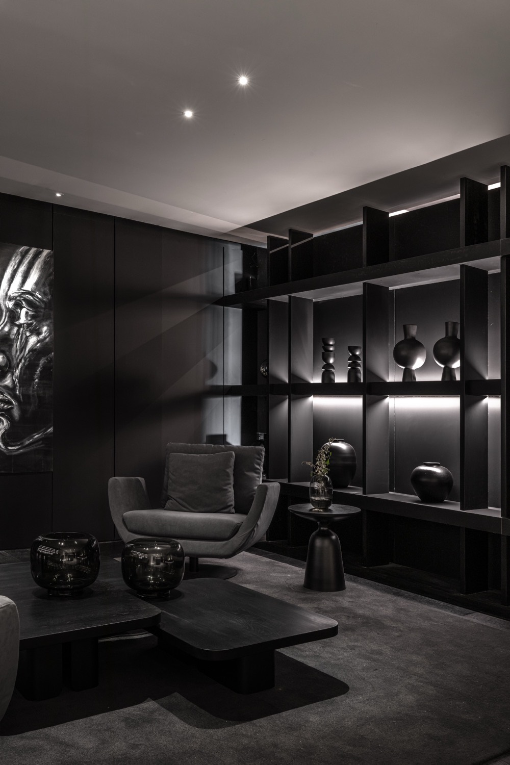Estar con sillón gris, estantería negra iluminada y la obra central sobre el plano oscuro