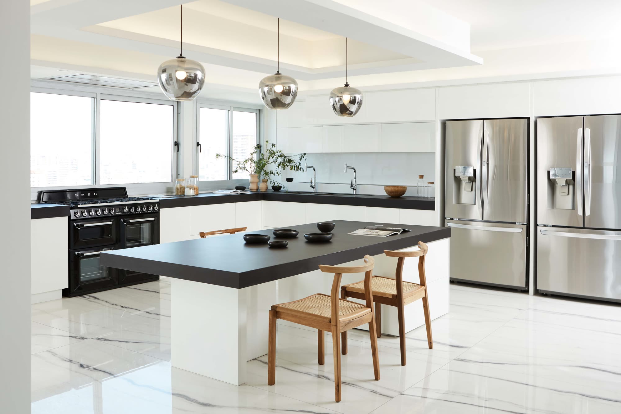 La cocina completa, con frentes blancos, mesada negra e isla central bajo tres colgantes de vidrio tonalizado, sobre piso simil marmol