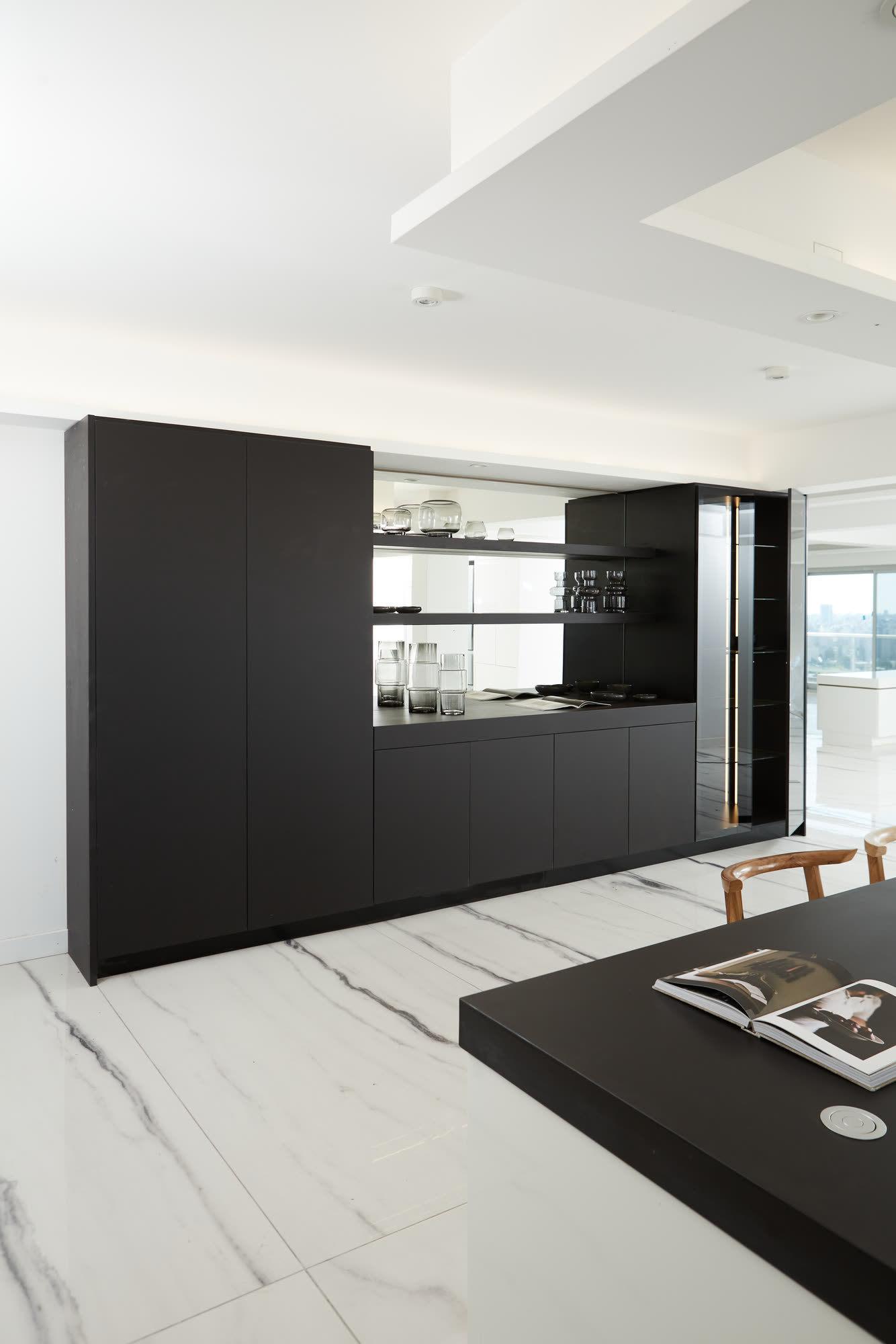Mueble de guardado revestido en Neolith negro a plena altura, con un sector abierto de estantes y una vitrina vidriada iluminada