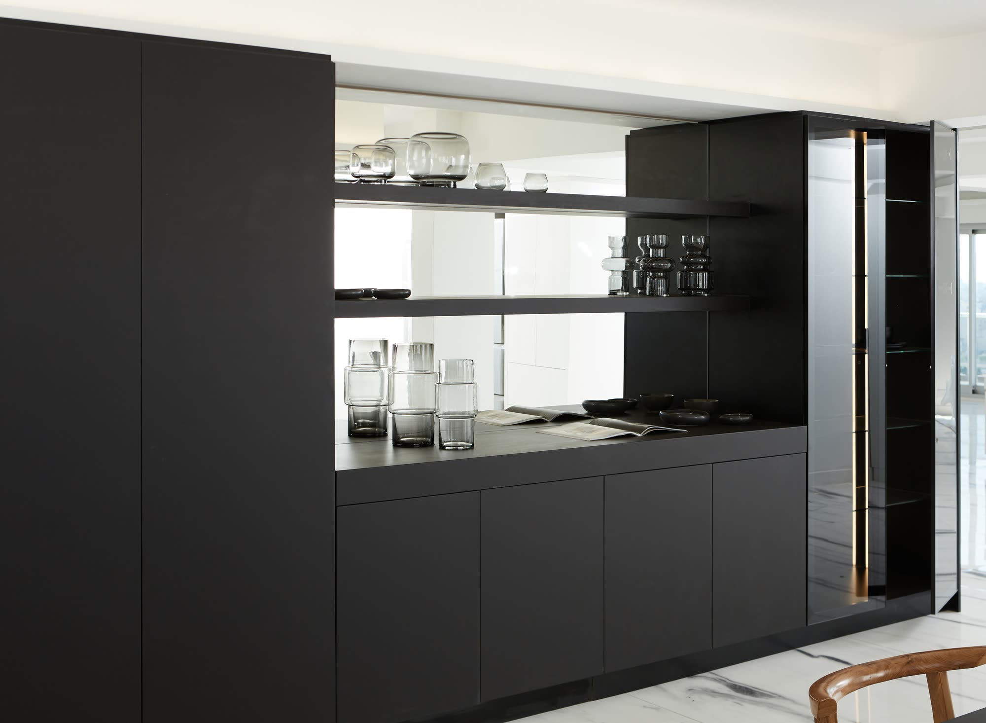 Detalle del mueble de Neolith negro: estantes abiertos sobre fondo espejado, mesada baja y vitrina de vidrio tonalizado con iluminacion lineal