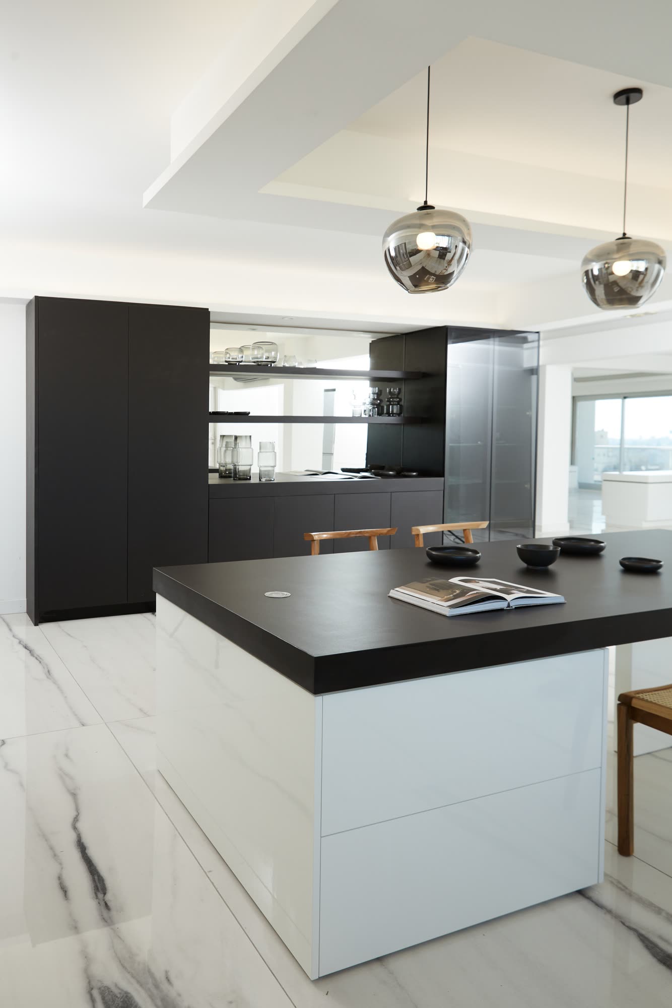 La isla de frentes claros y mesada de Neolith negro, con el mueble revestido en el mismo material y la vitrina vidriada al fondo