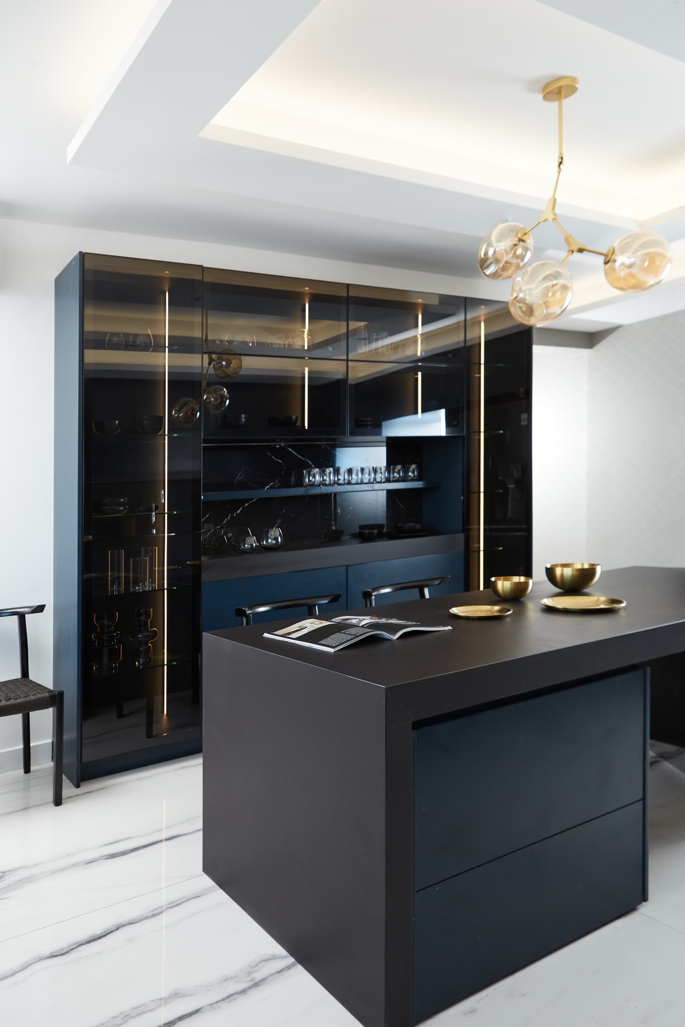 Mueble vitrina de vidrio tonalizado con iluminacion vertical de bronce, enfrentado a la isla negra
